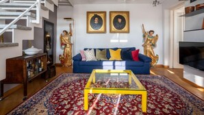 A living room with a blue sofa, a glass coffee table, and a staircase with white railings. - La Rocchetta 1915 by Interhome (Cortazzone)