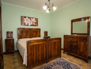 Ein Schlafzimmer mit einem hölzernen Bett, einem Schminktisch, einem Spiegel und einem Blumenbild an der Wand.