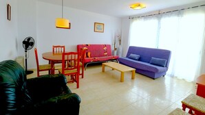 Una sala de estar con un sofá rojo, un sofá morado, una mesa de centro de madera, una mesa de comedor con sillas y un sofá de cuero negro.