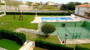 Una cancha de tenis con piscina, rodeada de césped y setos bien cuidados.