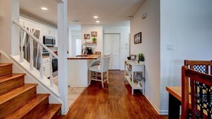 A modern kitchen with white cabinets, a wooden staircase, and a dining area with a white table and chairs. - 7South home across street from Lake Hamilton (Hot Springs)