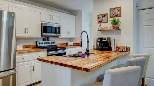 A kitchen with white cabinets, a wooden island, stainless steel appliances, and a coffee maker. - 7South home across street from Lake Hamilton (Hot Springs)