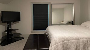 Ein Schlafzimmer mit einem Bett, einem Fernseher, einem Fenster mit Jalousien und einem Spiegel.