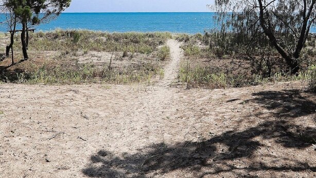 En stig som leder från stranden ner till havet, med sparsam växtlighet och en klar himmel.