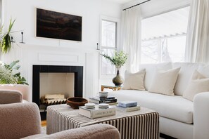 Una sala de estar con chimenea, un sofá, una mesa de centro con libros y un cuadro en la pared.