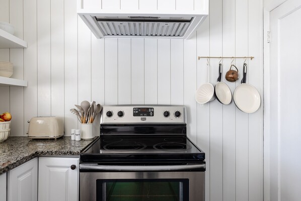 Una cocina con armarios blancos, estufa de acero inoxidable, un tostador y un colgador para ollas.