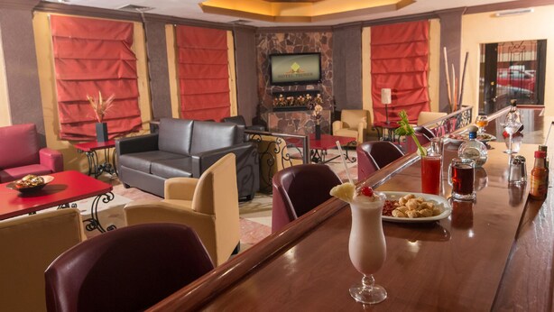 A hotel bar area with leather seating, a television, and a bar counter with drinks and condiments. - Hotel Premier (Hermosillo)