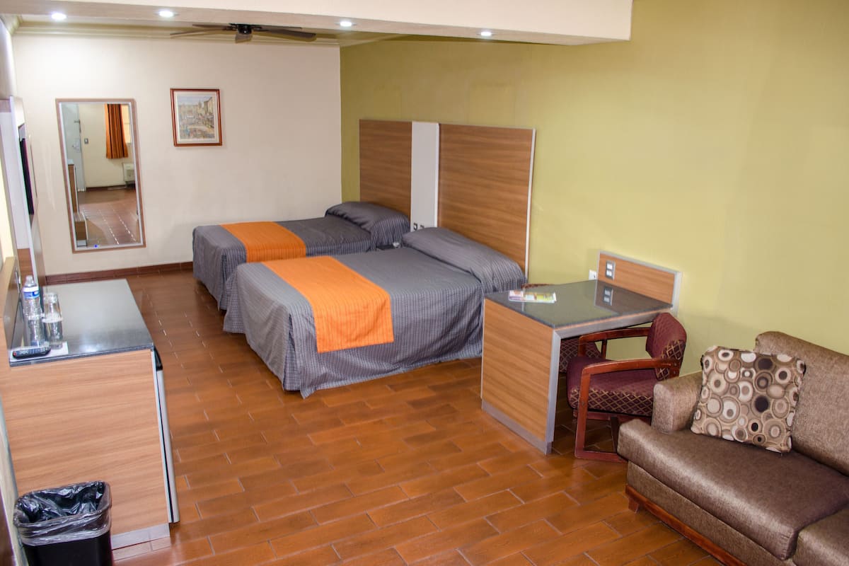 A hotel room with two beds, a desk, a chair, and a sofa.