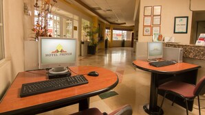 A hotel lobby with two computer stations, each with a monitor displaying the hotel's name, a keyboard, and a mouse. There are chairs and a reception desk with a computer and some items on it. - Hotel Premier (Hermosillo)