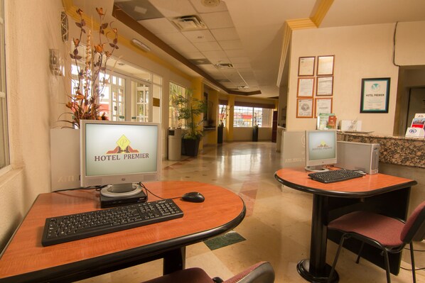 A hotel lobby with two computer stations, each with a monitor displaying the hotel's name, a keyboard, and a mouse. There are chairs and a reception desk with a computer and some items on it. - Hotel Premier (Hermosillo)