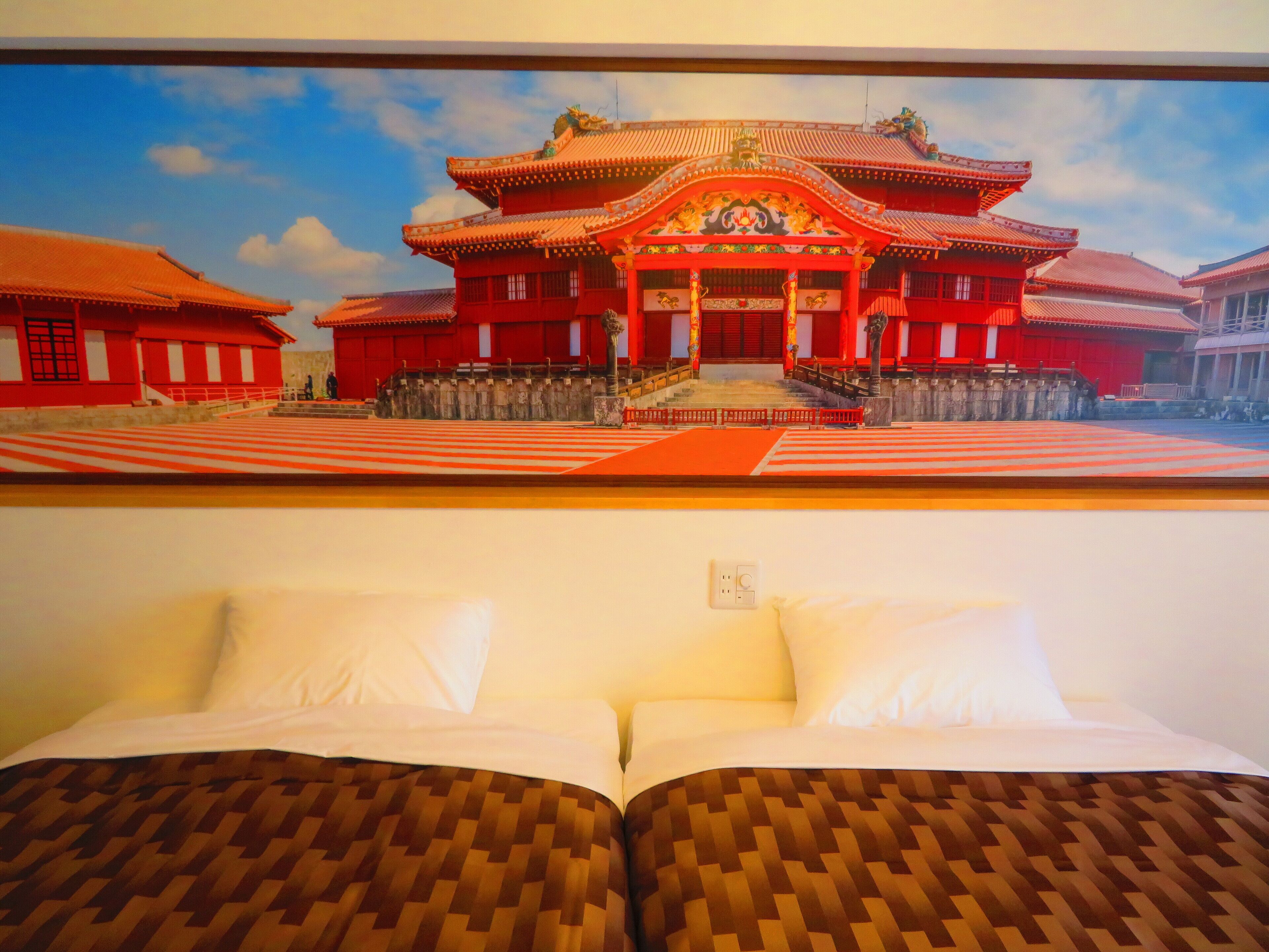 A hotel room with a bed, white pillows, and a view of a traditional red building with a decorative entrance.