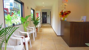 Un espace d’accueil d’hôtel avec des chaises en plastique blanches, des plantes en pot et un comptoir d’accueil en bois.