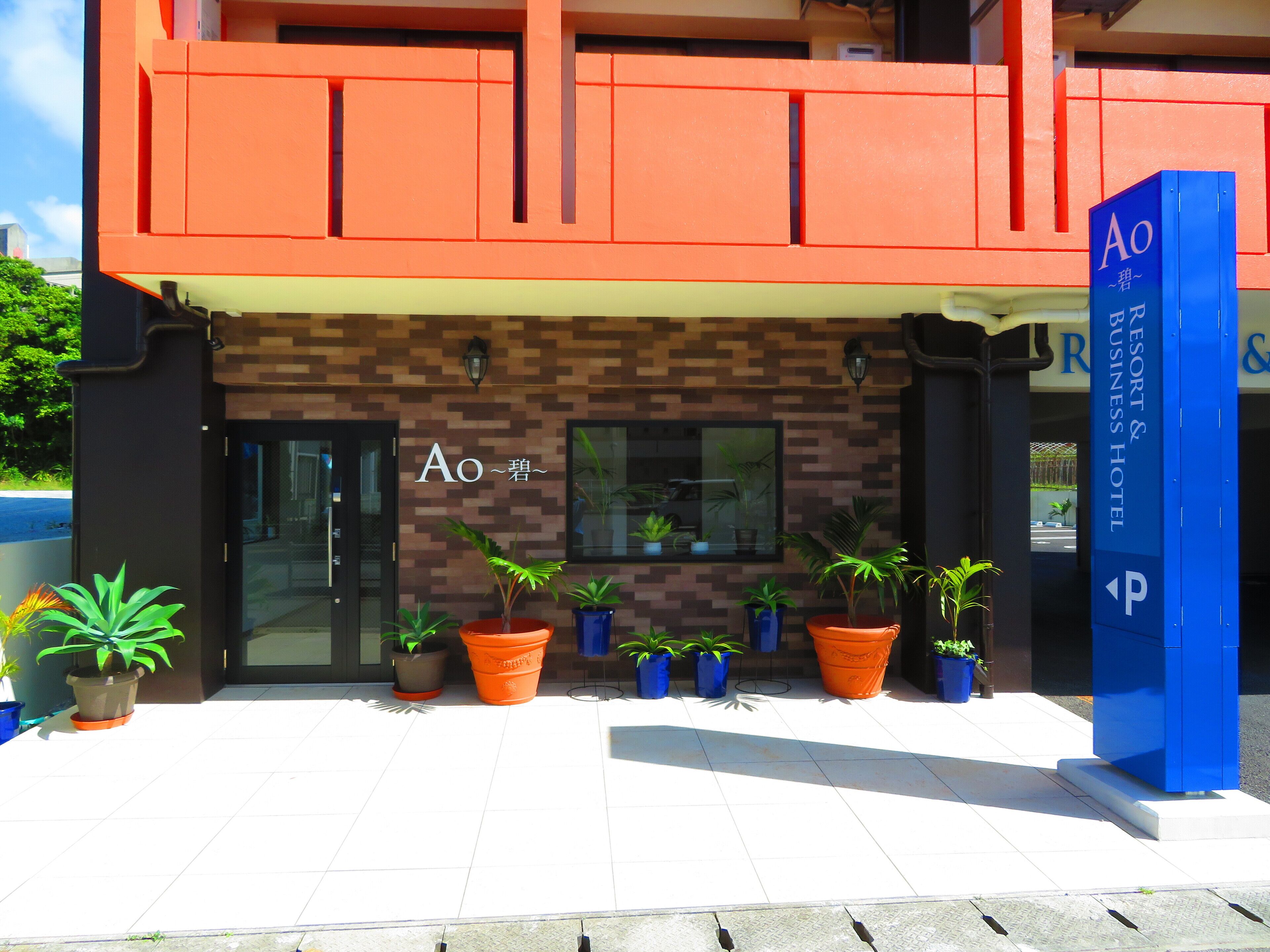 Entrada de un hotel con diseño moderno, destacando un letrero con el nombre 'Ao' y una señalización azul para estacionamiento.