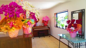 Une pièce avec un piano, un miroir et plusieurs compositions florales.