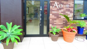 Une entrée d’immeuble avec une porte en verre, des plantes en pot et une enseigne avec des caractères japonais.