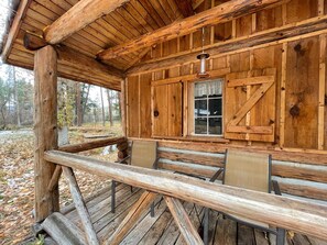 A rustic cabin with a wooden exterior, a porch with benches, and a window with curtains. - The Holmestead - Dry Cabin (Frenchtown)