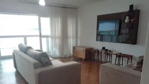 Una sala de estar con dos sofás, una mesa de centro, un televisor montado en la pared y una ventana con cortinas.