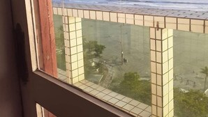 Vista desde una ventana con vista a una masa de agua y formas de terreno distantes, un balcón con tejas y un vistazo al interior.