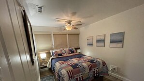 Ein Schlafzimmer mit Bett, Deckenventilator, Nachttisch und einem Fenster mit Jalousien.