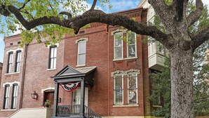 A two-story brick building with a front porch, a flag, and a staircase leading to the second floor. - On Lafayette Square, Heated Pool Access (Savannah)