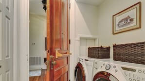 A laundry room with two front-loading washing machines, a wooden door, and a framed picture on the wall. - On Lafayette Square, Heated Pool Access (Savannah)