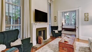 A spacious living room with a fireplace, a television, and a bed in the background. - On Lafayette Square, Heated Pool Access (Savannah)