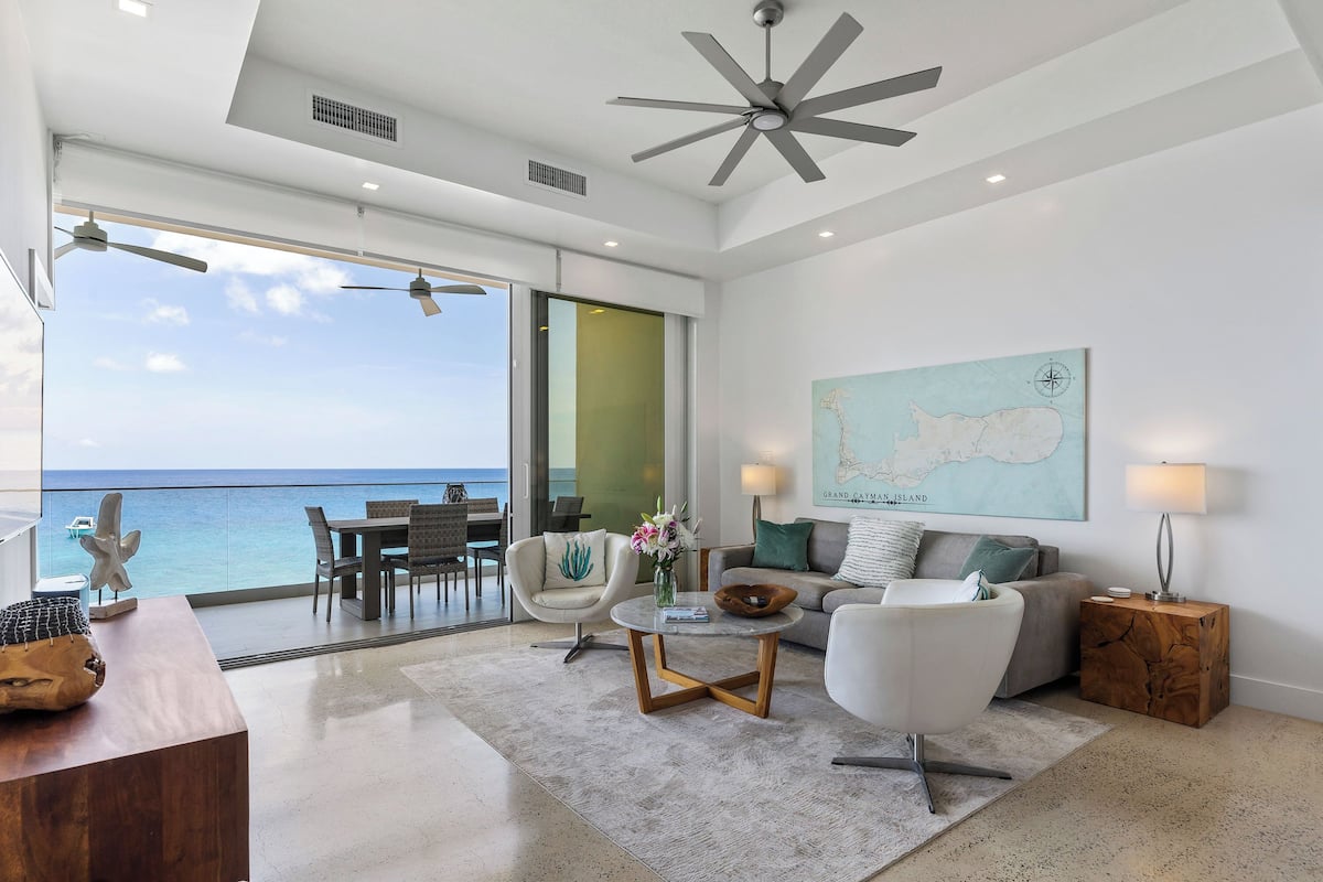 A modern living room with a large window overlooking the sea, a ceiling fan, and a map on the wall.