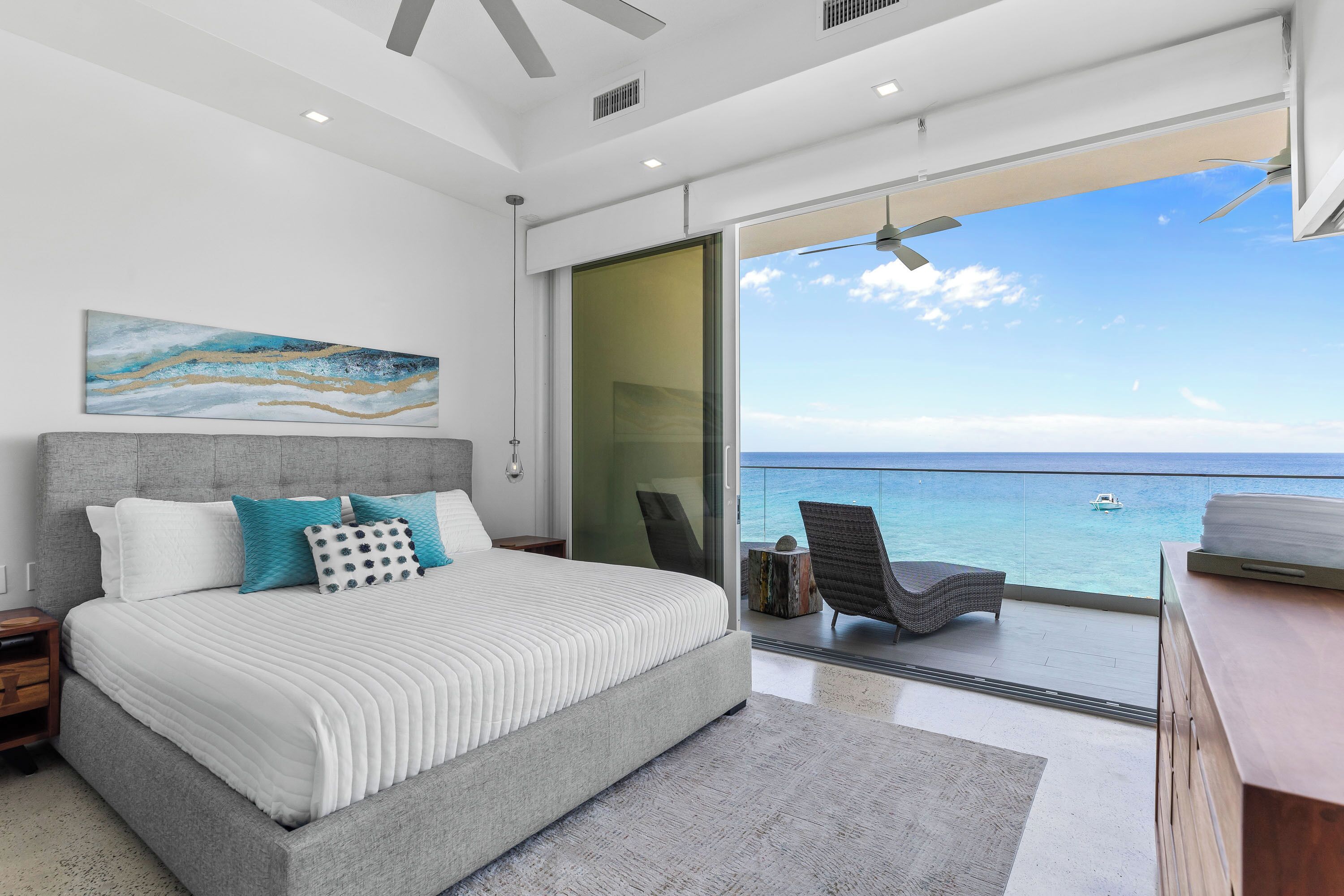 A modern bedroom with a large bed, a view of the ocean, and a balcony with a chair.