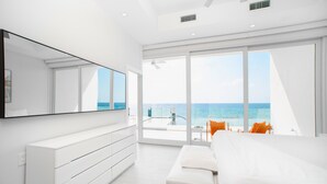 Un dormitorio moderno con una cama grande, un aparador blanco, un espejo amplio y un balcón con vista al océano.