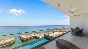 Un balcón con vista al mar, una piscina y mobiliario de exterior.