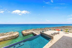 Ein Poolbereich mit klarem, blauem Wasser, einer felsigen Küstenlinie und Blick auf den Ozean.