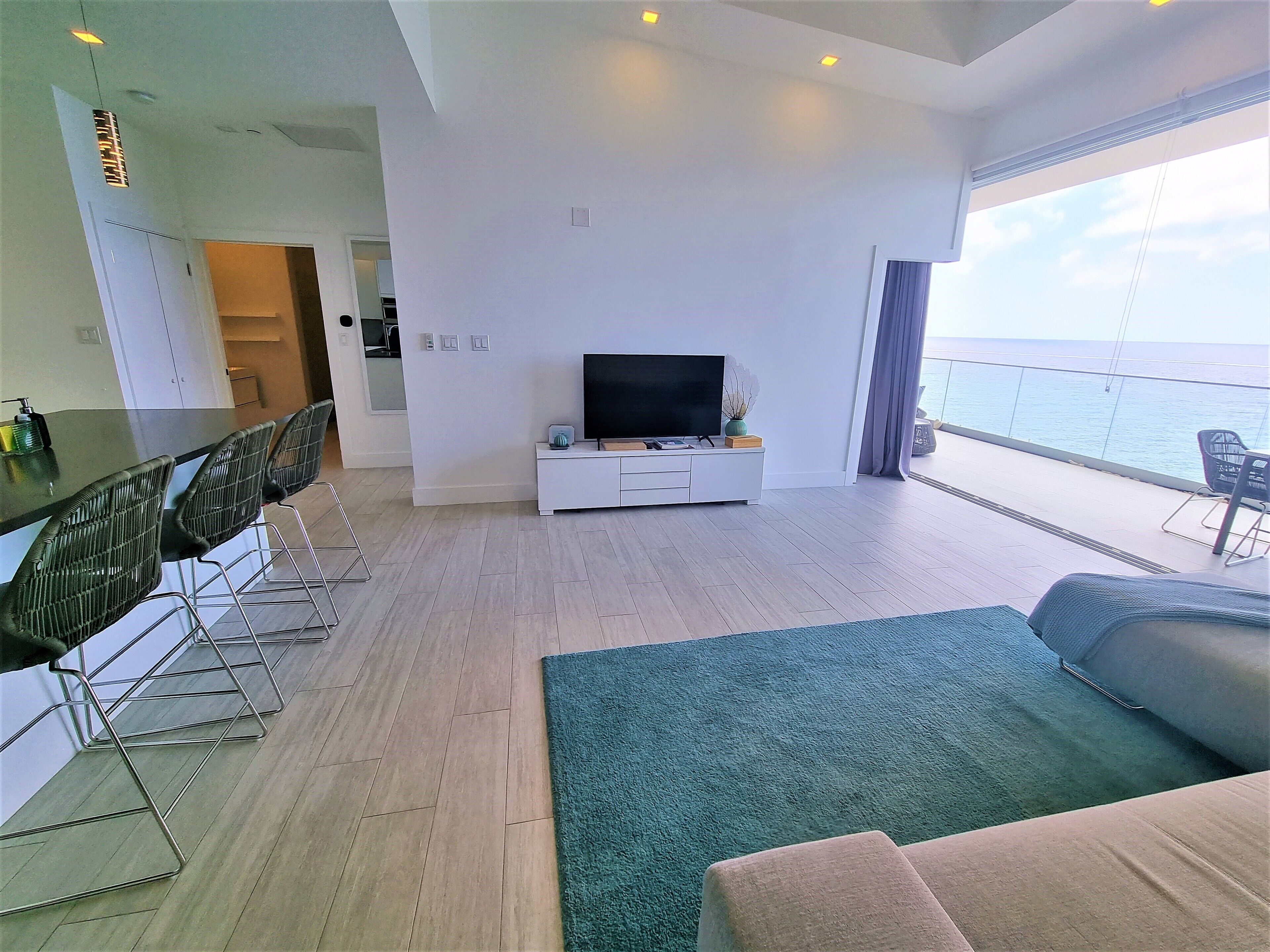A modern living room with a TV, seating, and a view of the sea.