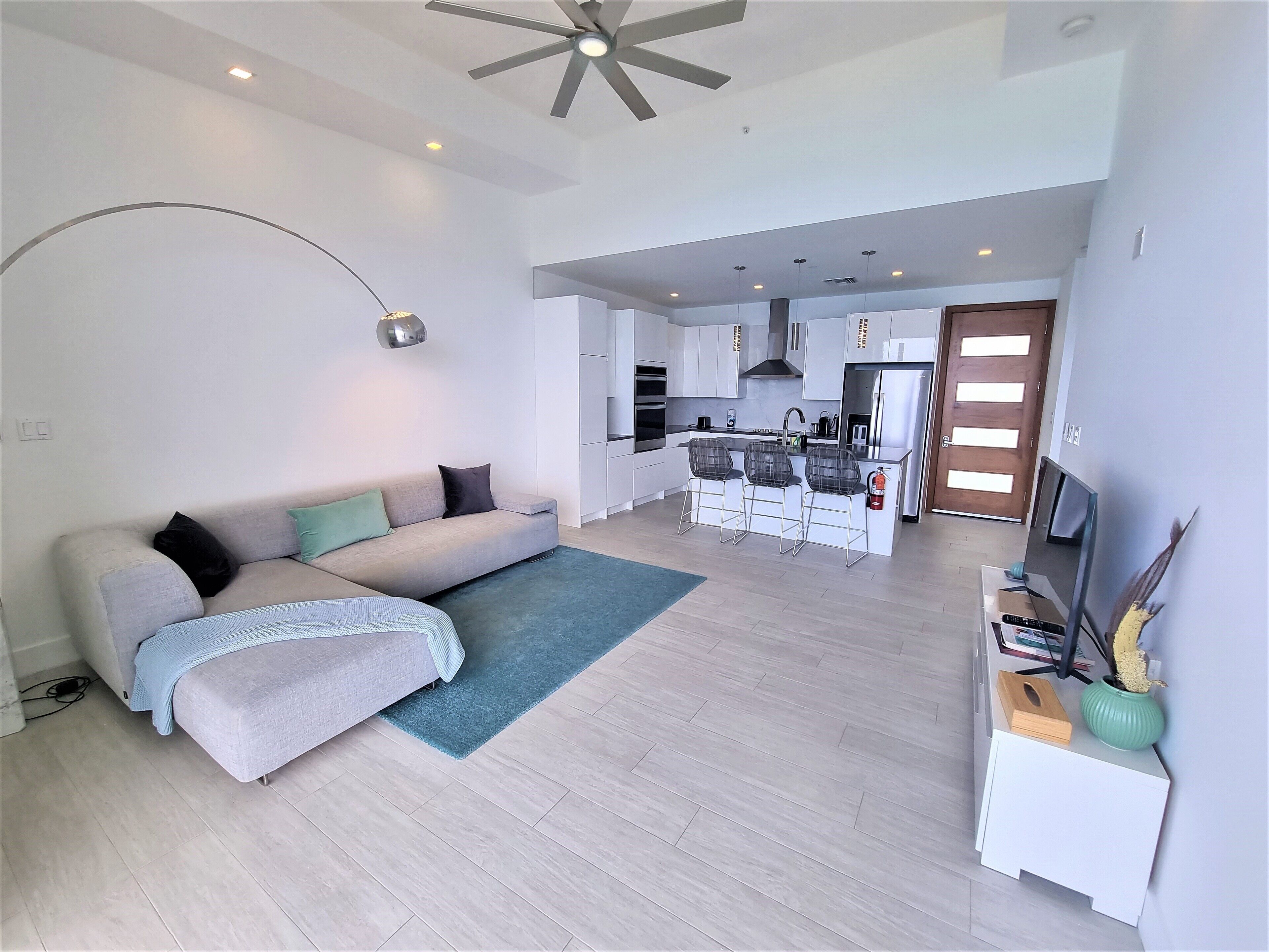 A modern living room with a sofa, a coffee table, and a dining area with a kitchen in the background.