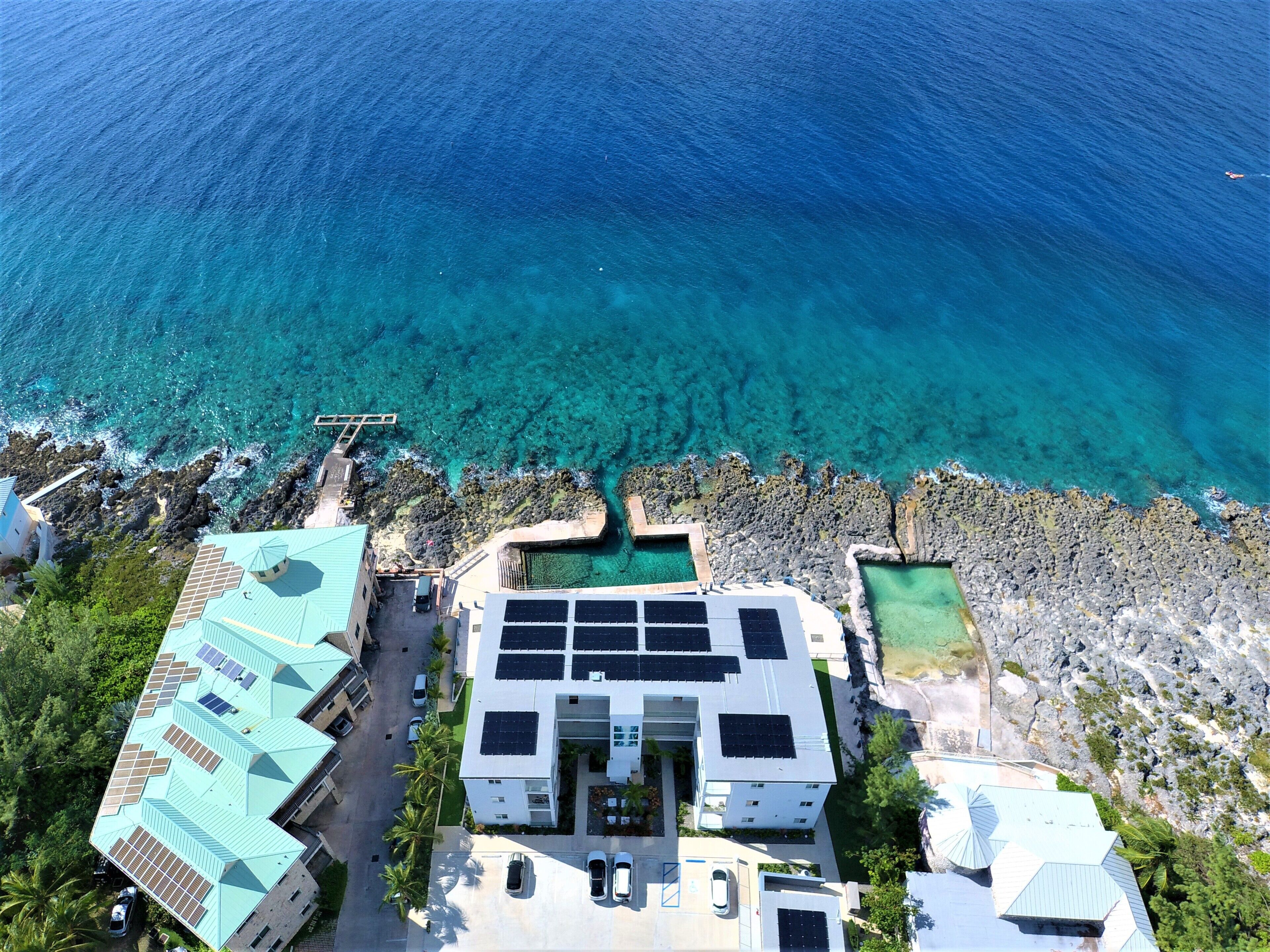 Vista aérea de una propiedad costera con piscina, paneles solares y un litoral rocoso.