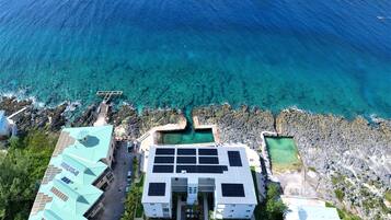Vista aérea de una propiedad costera con piscina, paneles solares y un litoral rocoso.