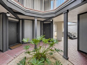 A modern building with a courtyard featuring a central plant, a staircase, and a door marked with the number 107. - 3697 Orlando Vacational Apartment 1st floor near Universal Studios (Orlando)