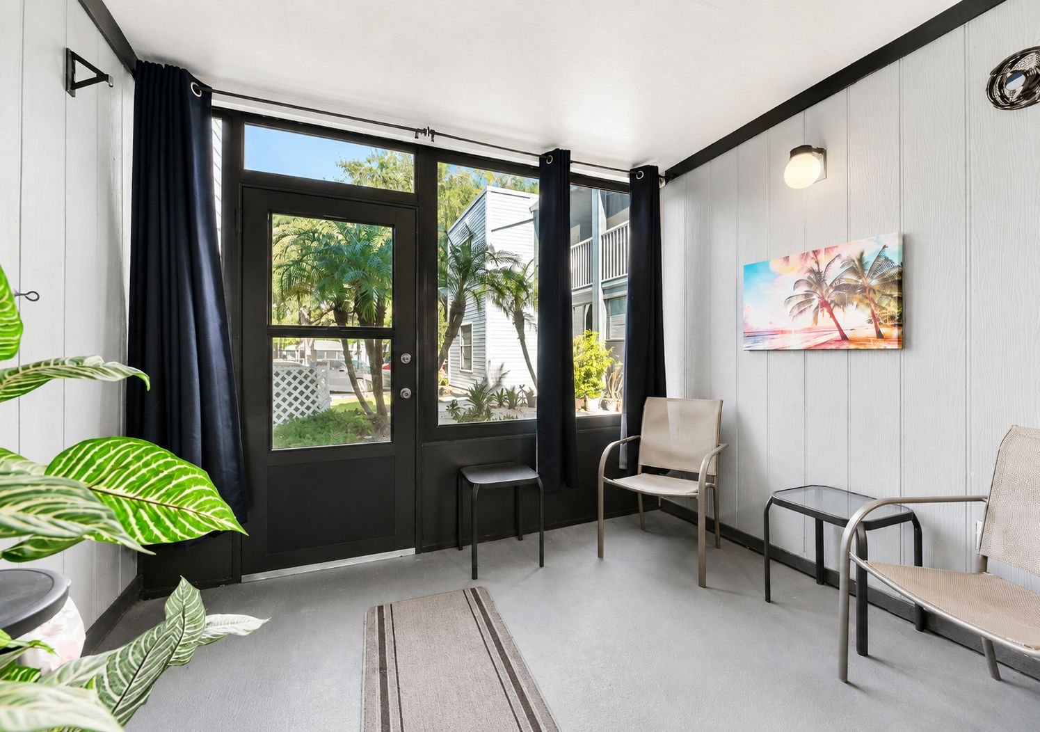 Quarto com porta de vidro deslizante, duas cadeiras, um quadro e um vaso de planta.