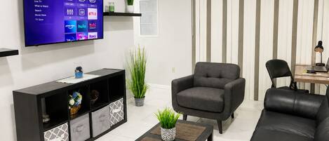 Un salon moderne doté d’un téléviseur à écran plat, d’un canapé noir, d’un fauteuil gris, d’une table basse et d’un meuble TV noir agrémenté d’objets décoratifs.