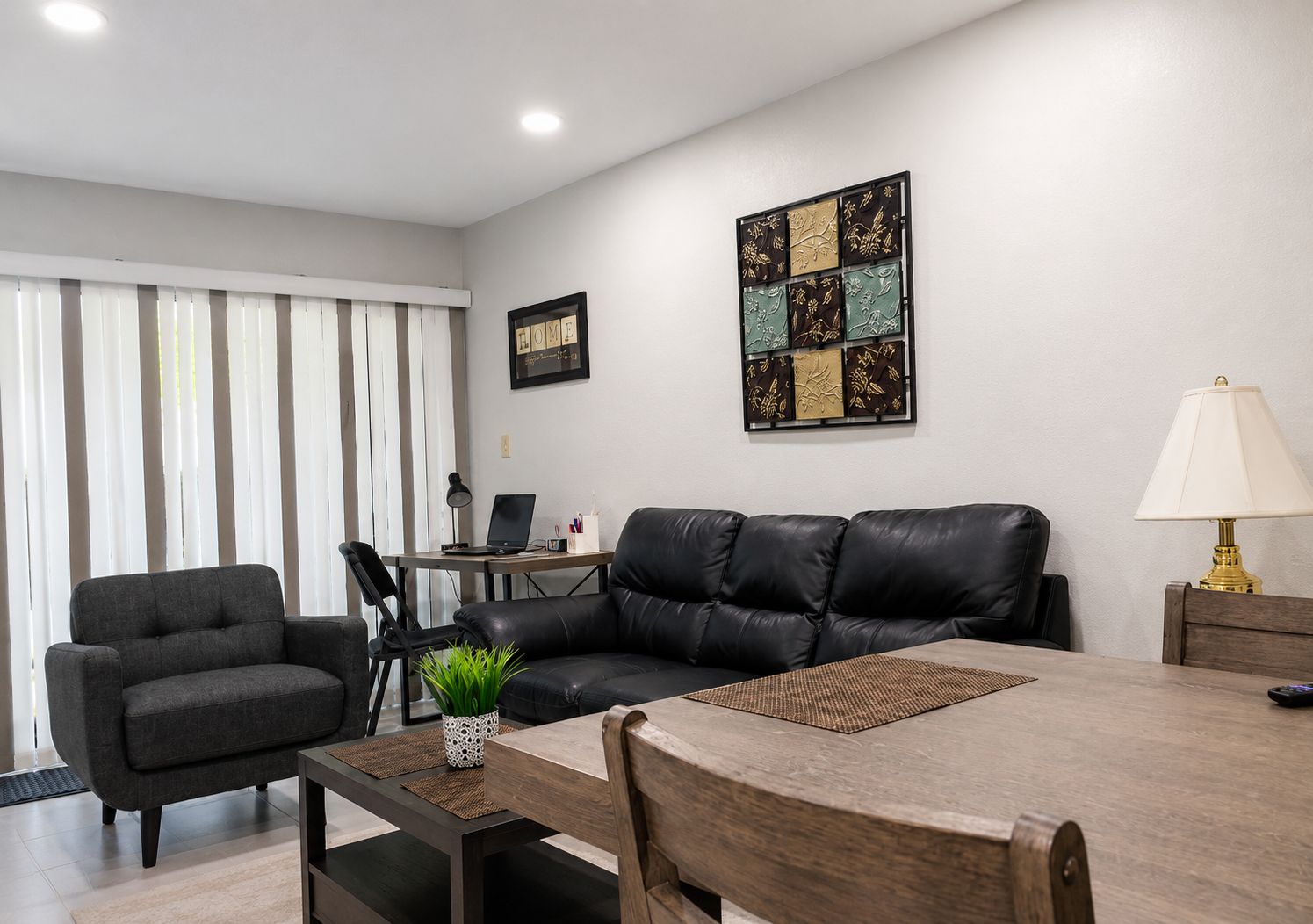 Uma sala de estar moderna com um sofá de couro, uma mesa de jantar e um laptop sobre uma escrivaninha.
