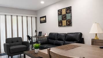 Uma sala de estar moderna com um sofá de couro, uma mesa de jantar e um laptop sobre uma escrivaninha.