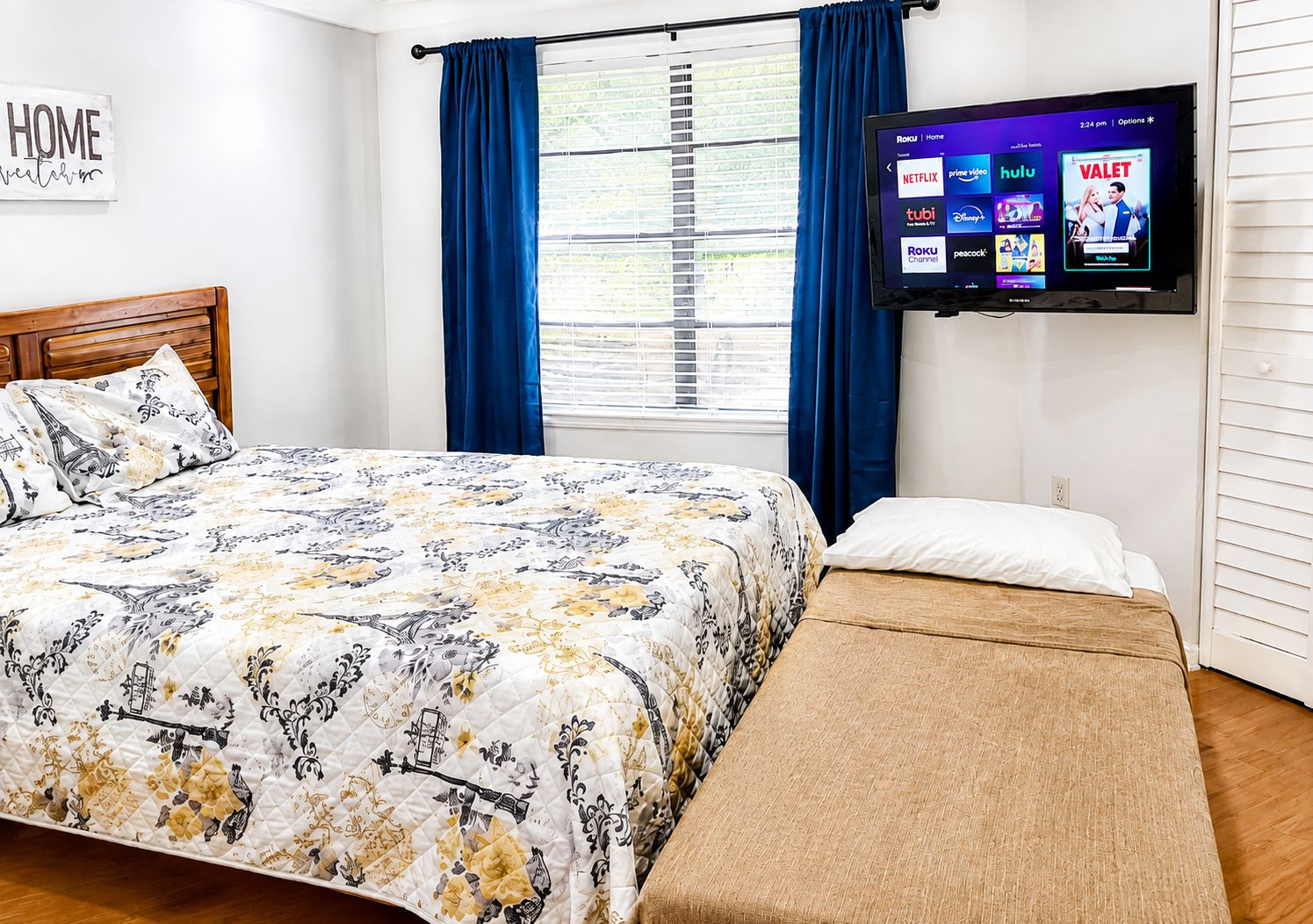 Una habitación de hotel con una cama, un televisor montado en la pared y una ventana con cortinas.