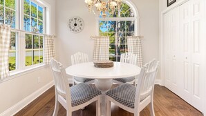 A dining room with a round table, white chairs, a chandelier, and a large window with curtains. - Pet Friendly Long-Term Rental - 25 Day Min  - Fenced Backyard - Grill (St. James)