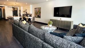 Una sala de estar moderna con un sofá seccional gris, una mesa de centro de vidrio y un televisor de pantalla plana montado en la pared.
