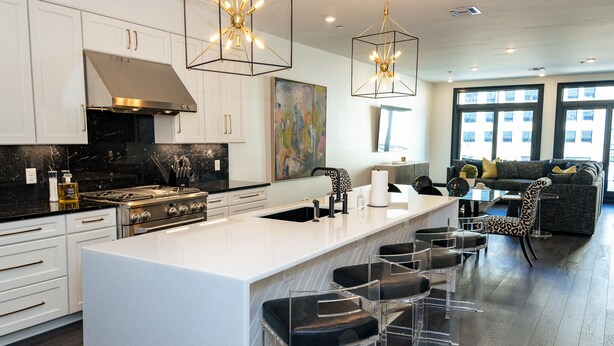 Una cocina moderna con una isla central, taburetes de bar y una zona de comedor con sofá y sillas.