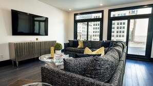 Un salón moderno con un sofá gris, una mesa de centro de cristal y un televisor de pantalla plana montado en la pared.