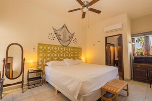 A hotel room with a bed, a ceiling fan, a decorative wall hanging, a bedside table, and a mirror. - ONE block from the beach at main st. (Loreto)
