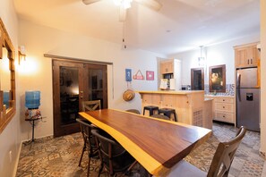 Una cocina con una mesa de madera, sillas, un dispensador de agua y un refrigerador.