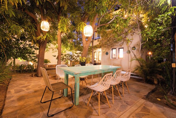 An outdoor dining area with a table and chairs, surrounded by trees and plants, under string lights. - ONE block from the beach at main st. (Loreto)