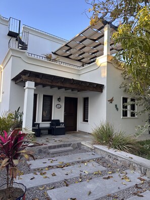 A white building with a covered patio, stone steps, and potted plants.