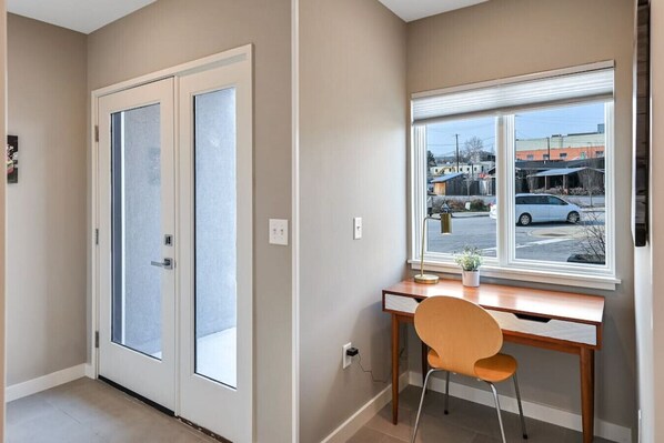 A room with a desk, chair, and a window with a view of a parking lot and buildings.